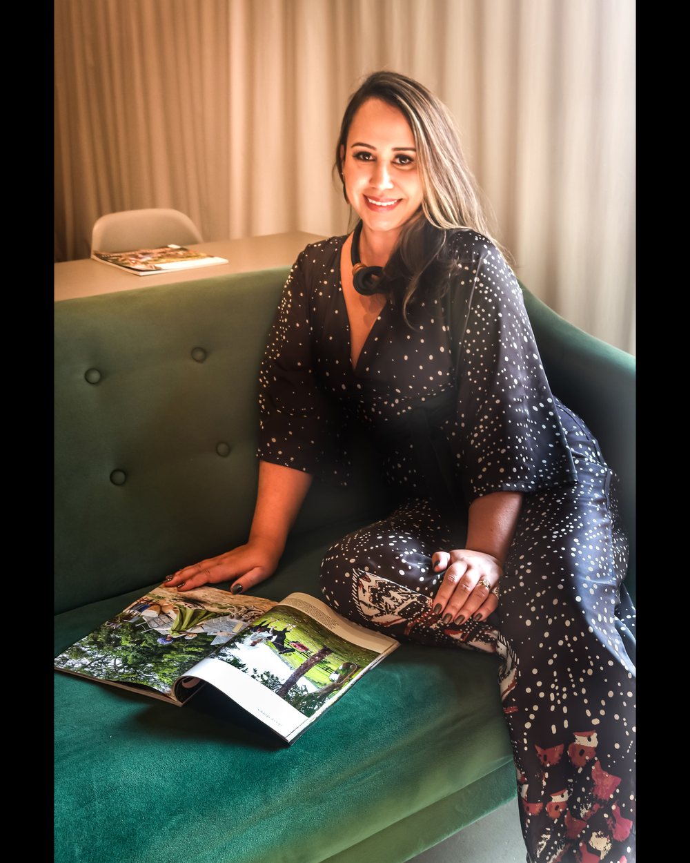Lígia Prette, arquiteta responsável pelos projetos de interiores, sentada em um sofá verde folheando uma revista de arquitetura